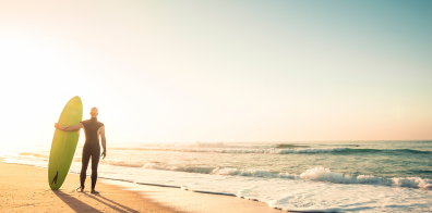 man on the beach holding a surfboard, looking at the ocean