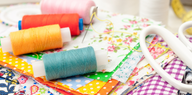 different coloured sewing threads, with one needle and many different fabrics and a pair of scissors