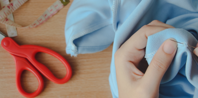 a person sewing a fabric using a sewing needle, with scissors and a measuring ruler in the background