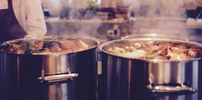 Two large pots of food steaming on a hob in a professional kitchen